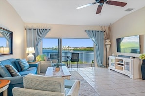 A living room with a sofa, chairs, a coffee table, a TV, and a balcony with a view.