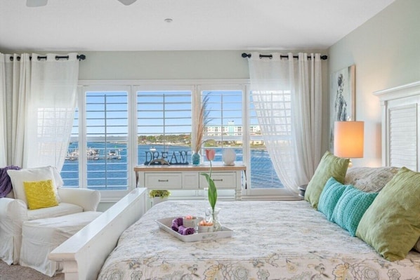 A bedroom with a bed, a desk, a chair, and a view of the sea.