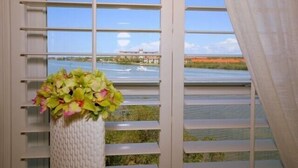 A window with horizontal blinds, a view of a body of water, and a white vase with flowers. - Beautiful Views! Water front! Two Bedrooms and Two Baths with free wifi and beach equipment (Indian Rocks Beach)