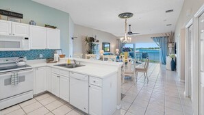 A kitchen with white cabinets, a microwave, and a stove. There is a dining area with a table and chairs, and a view of the ocean. - Beautiful Views! Water front! Two Bedrooms and Two Baths with free wifi and beach equipment (Indian Rocks Beach)