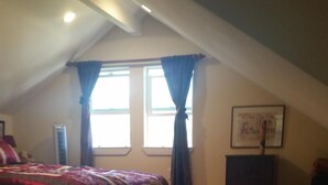 A bedroom with a large bed, a window with curtains, a framed picture on the wall, and a small table.