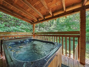 Ein Whirlpool unter einer Holzterrasse mit Blick auf eine bewaldete Landschaft.
