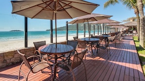 A wooden deck with tables and chairs under umbrellas, overlooking a beach. - Pietra Flat (Florianópolis)