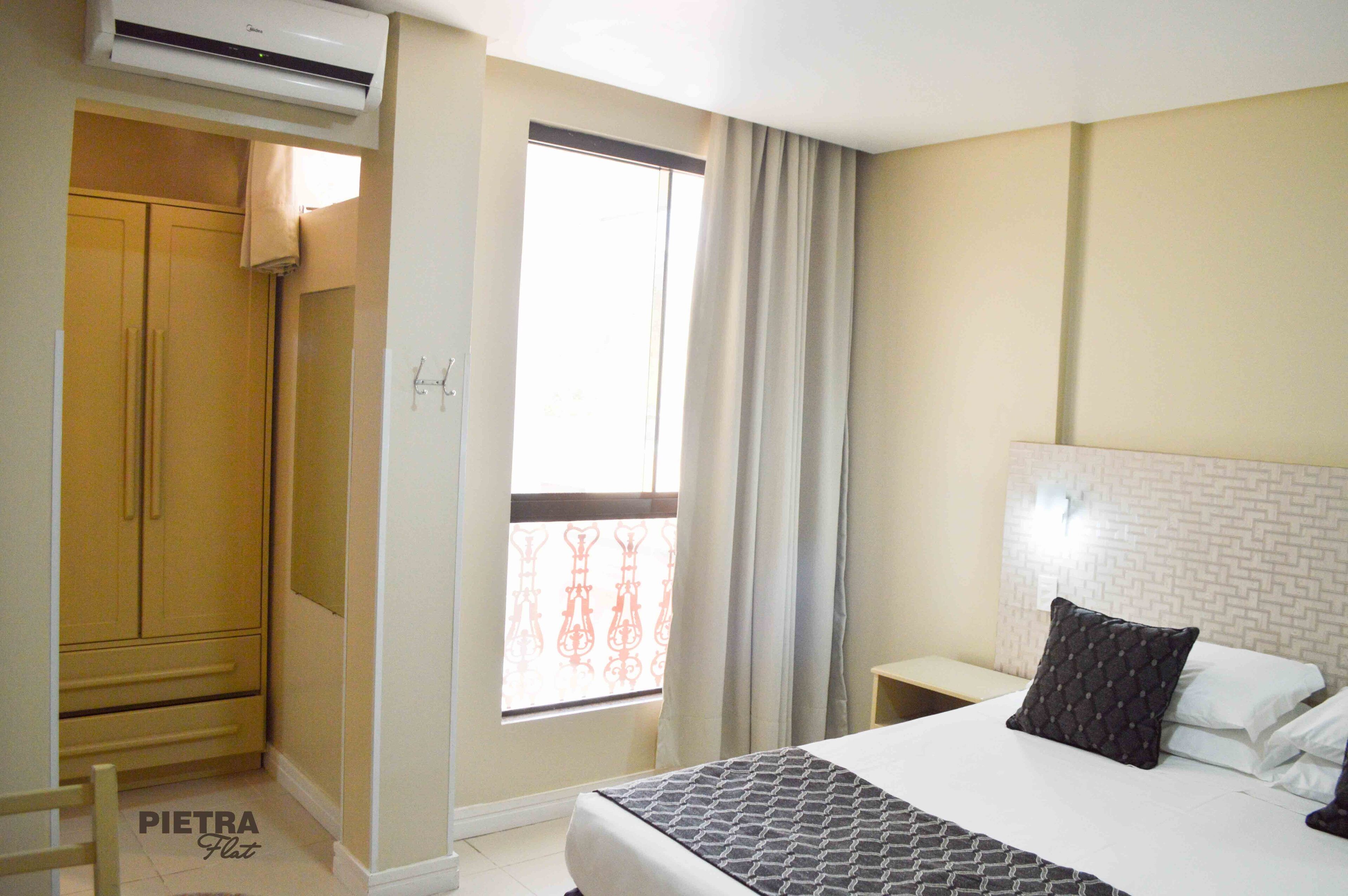 A bedroom with a bed, a nightstand, a wardrobe, and a window with curtains.