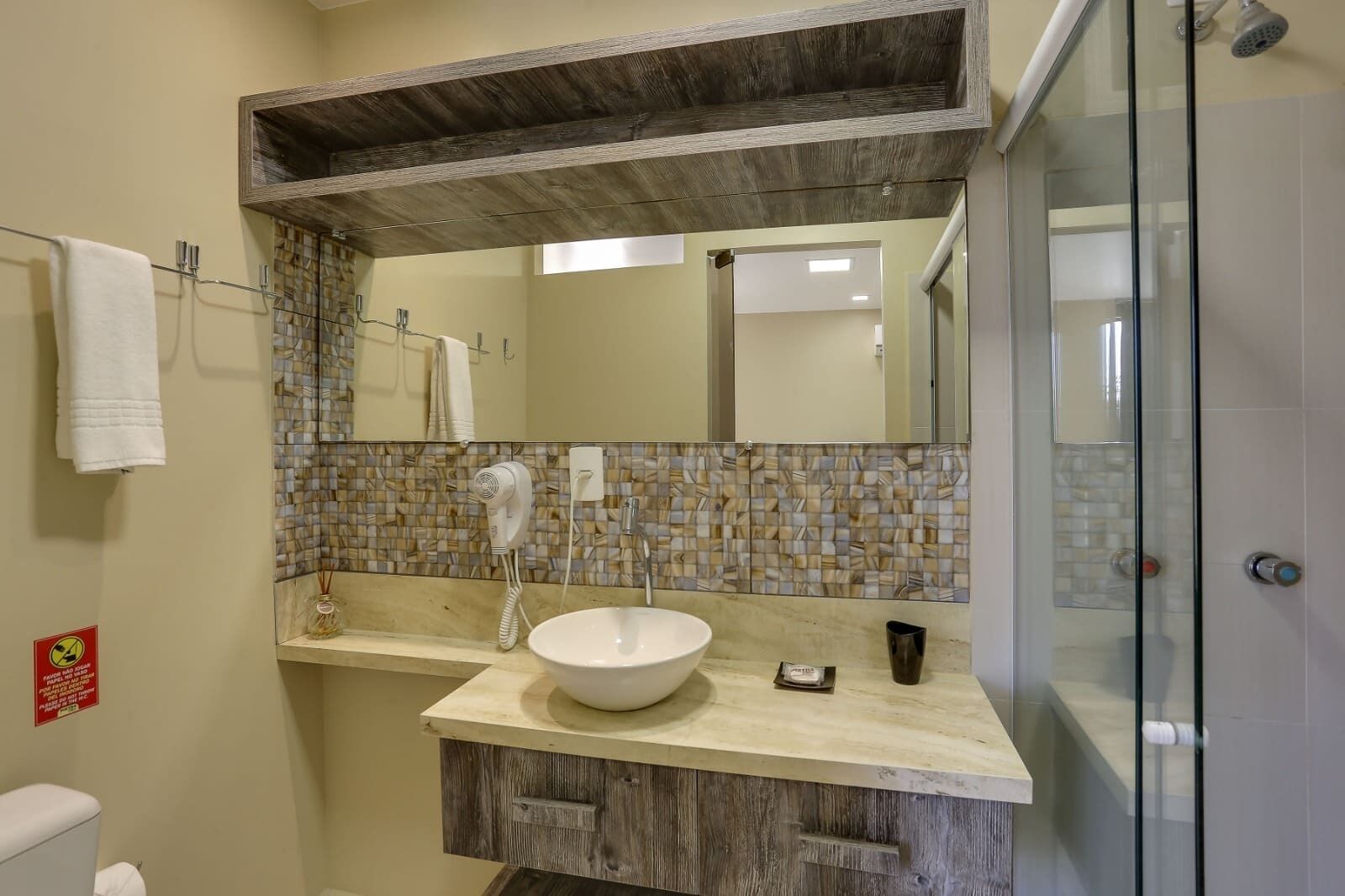 A bathroom with a wooden vanity, a white sink, a mirror above the vanity, and a shower area.