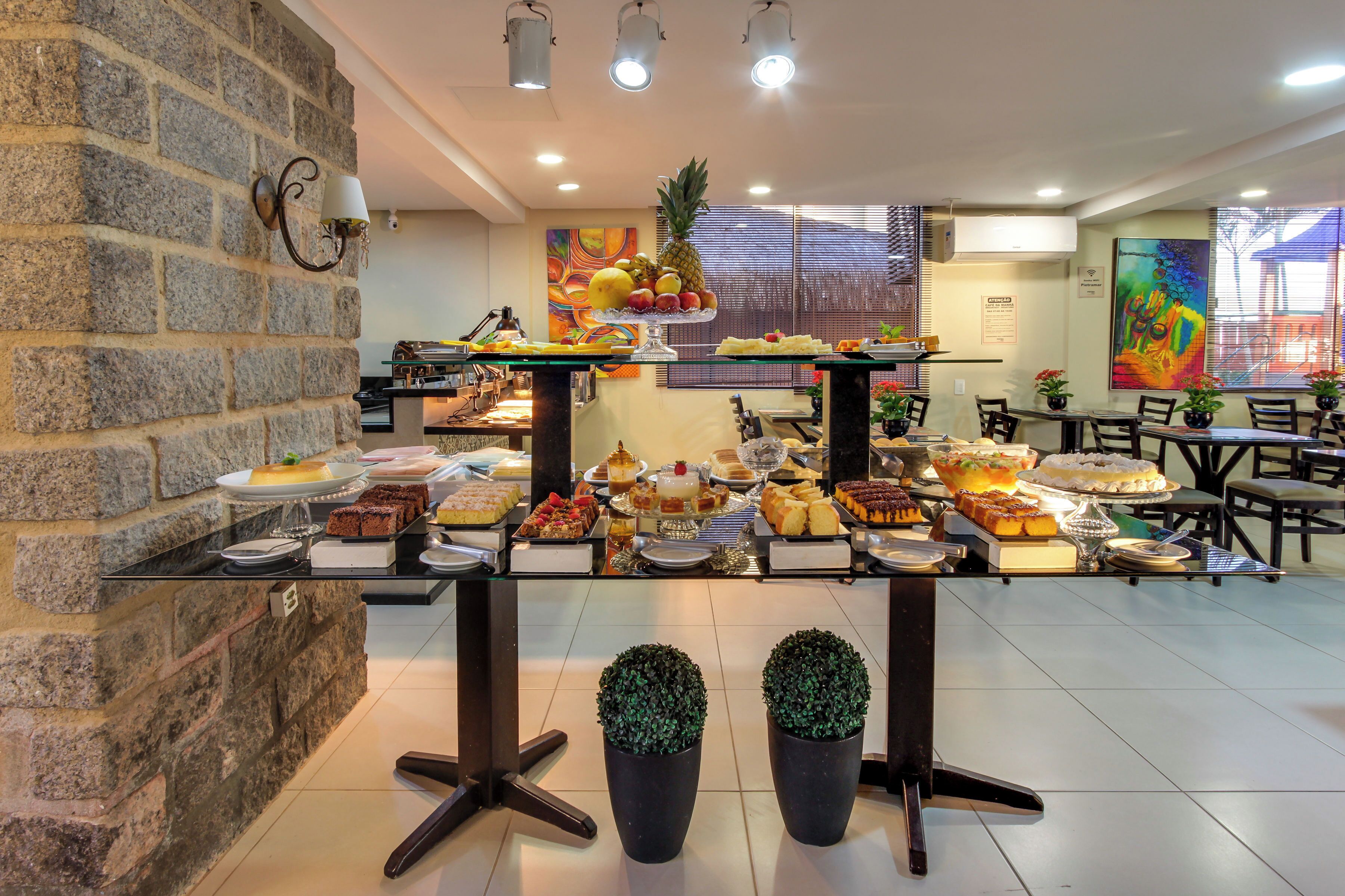 Un área de bufé con diversos postres y frutas, una pared de piedra e iluminación moderna.