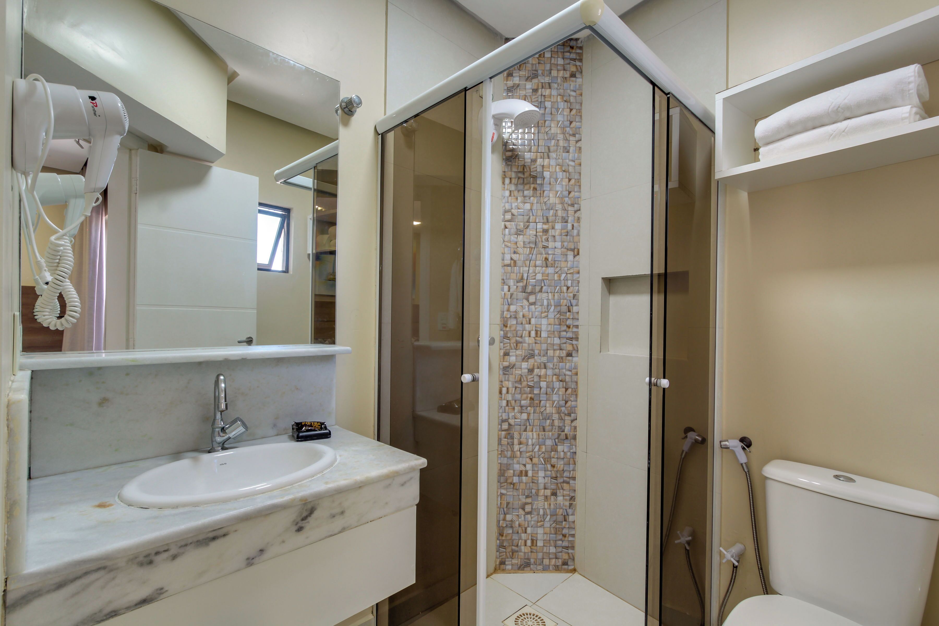 A bathroom with a marble sink, a hairdryer, a glass-enclosed shower, and a toilet.