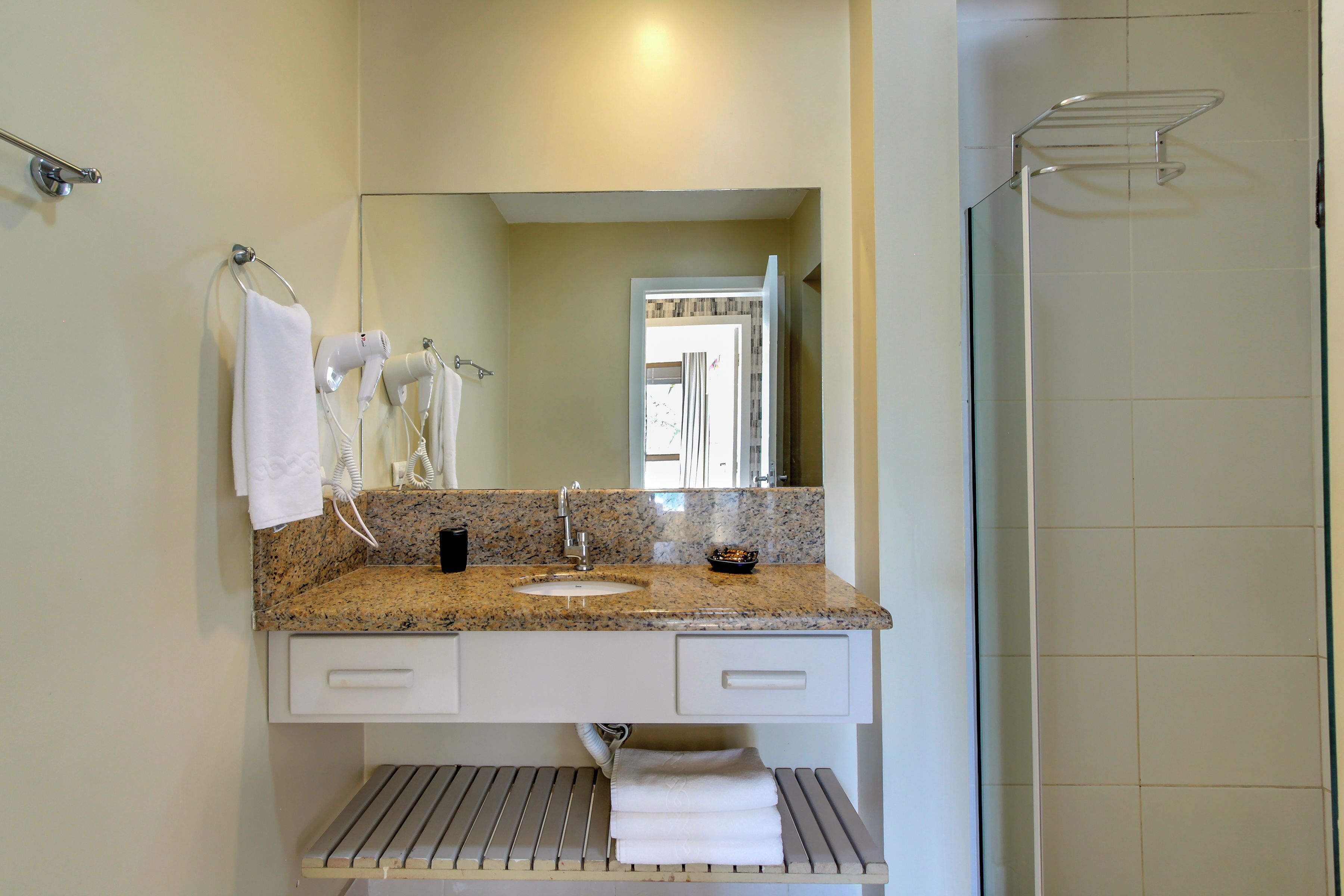 Une salle de bain avec un comptoir en granit, un lavabo, un miroir et un espace douche.