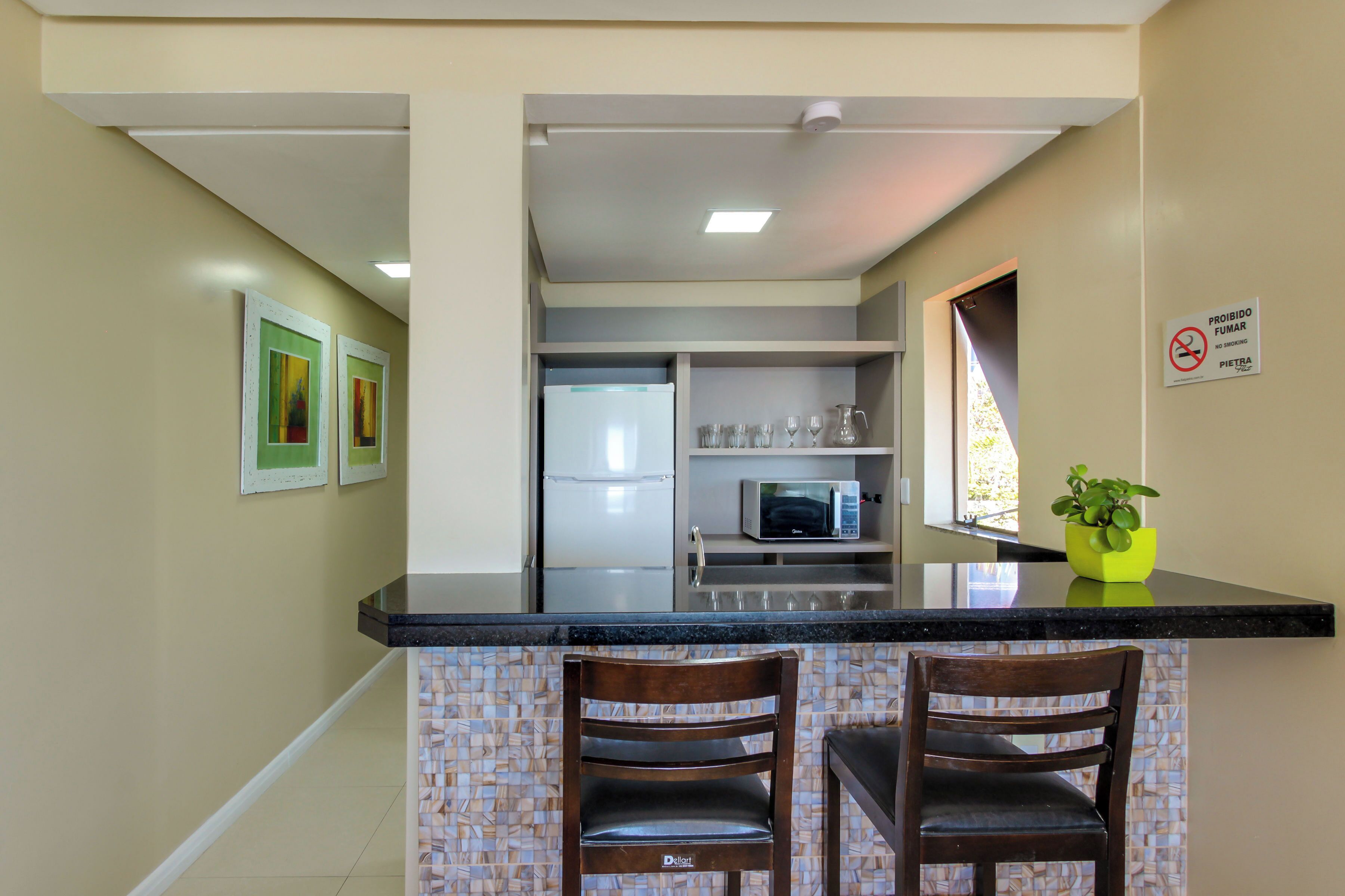 A kitchen with a black countertop, two wooden chairs, a microwave, and a refrigerator.