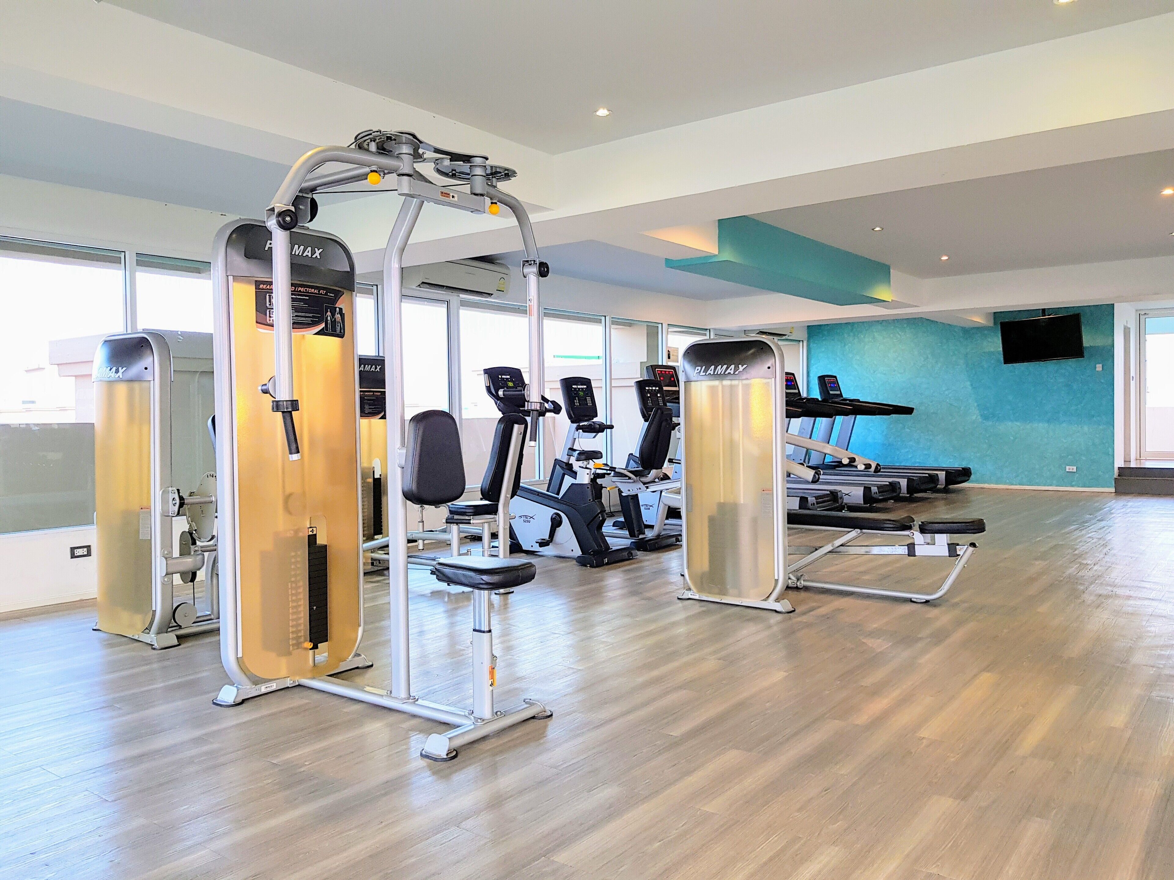 Un gimnasio moderno con diversos equipos de ejercicio, ventanas amplias y una pared de acento azul.