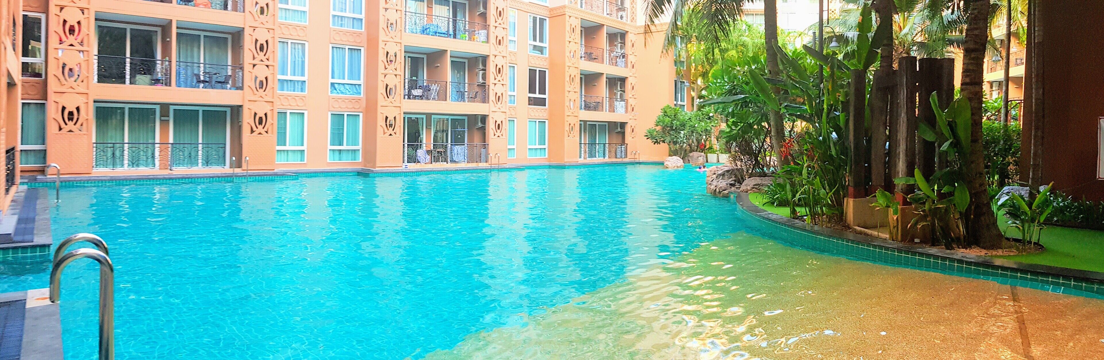 A hotel with a swimming pool, balconies with outdoor furniture, and lush greenery.