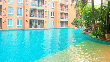 A hotel with a swimming pool, balconies with outdoor furniture, and lush greenery.