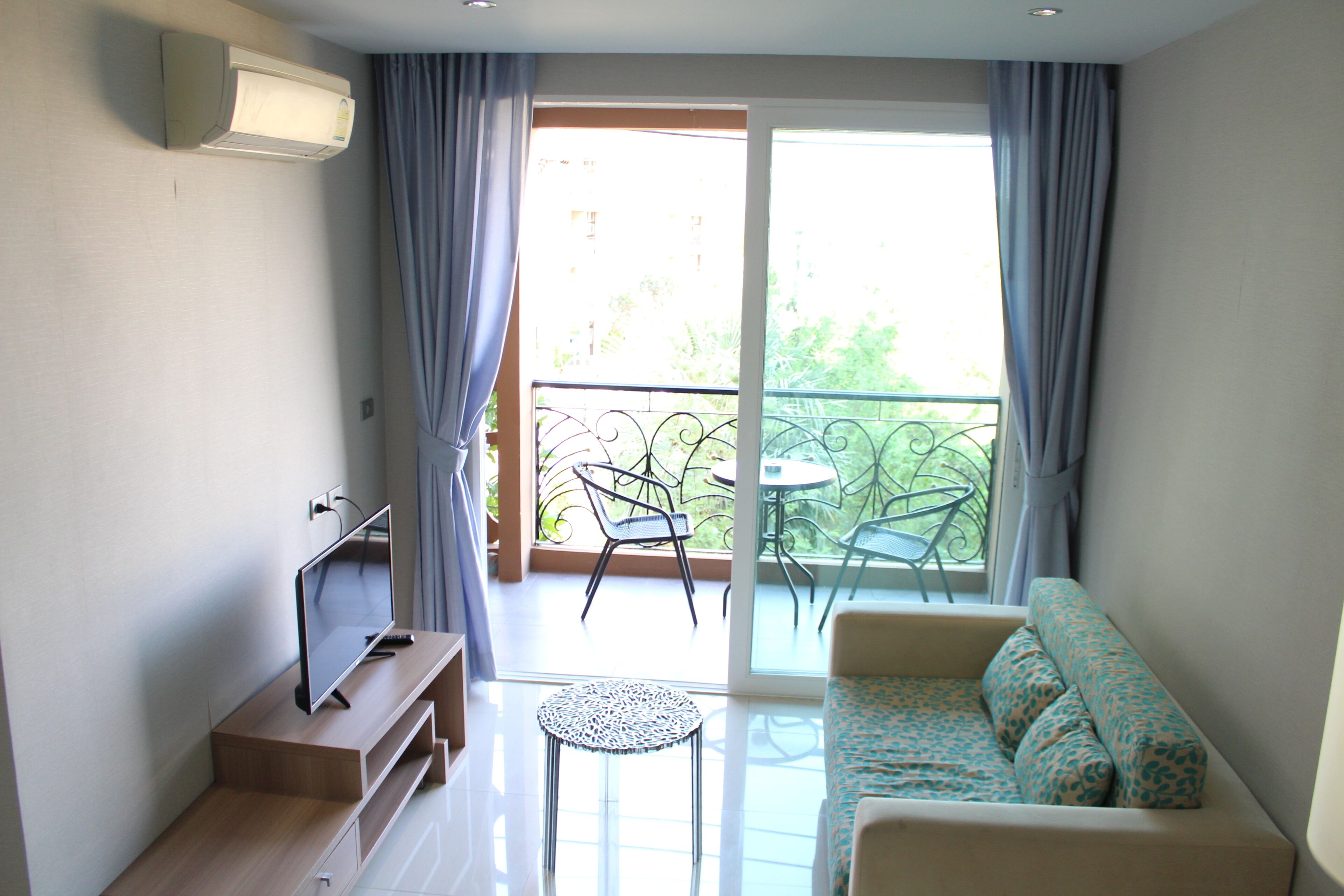 A modern living room with a sofa, a TV, a small table, and a balcony with chairs.
