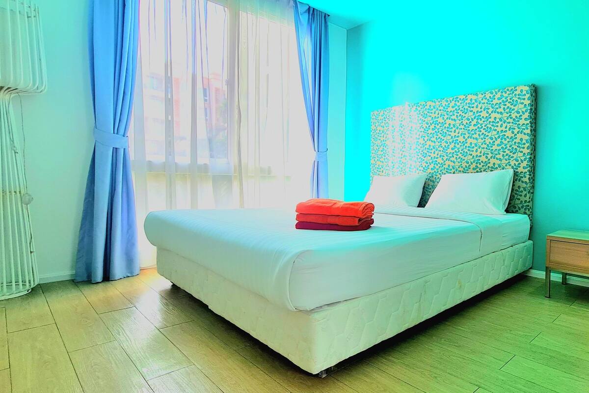 Une chambre à coucher avec un lit, une table de chevet en bois et une fenêtre avec des rideaux.