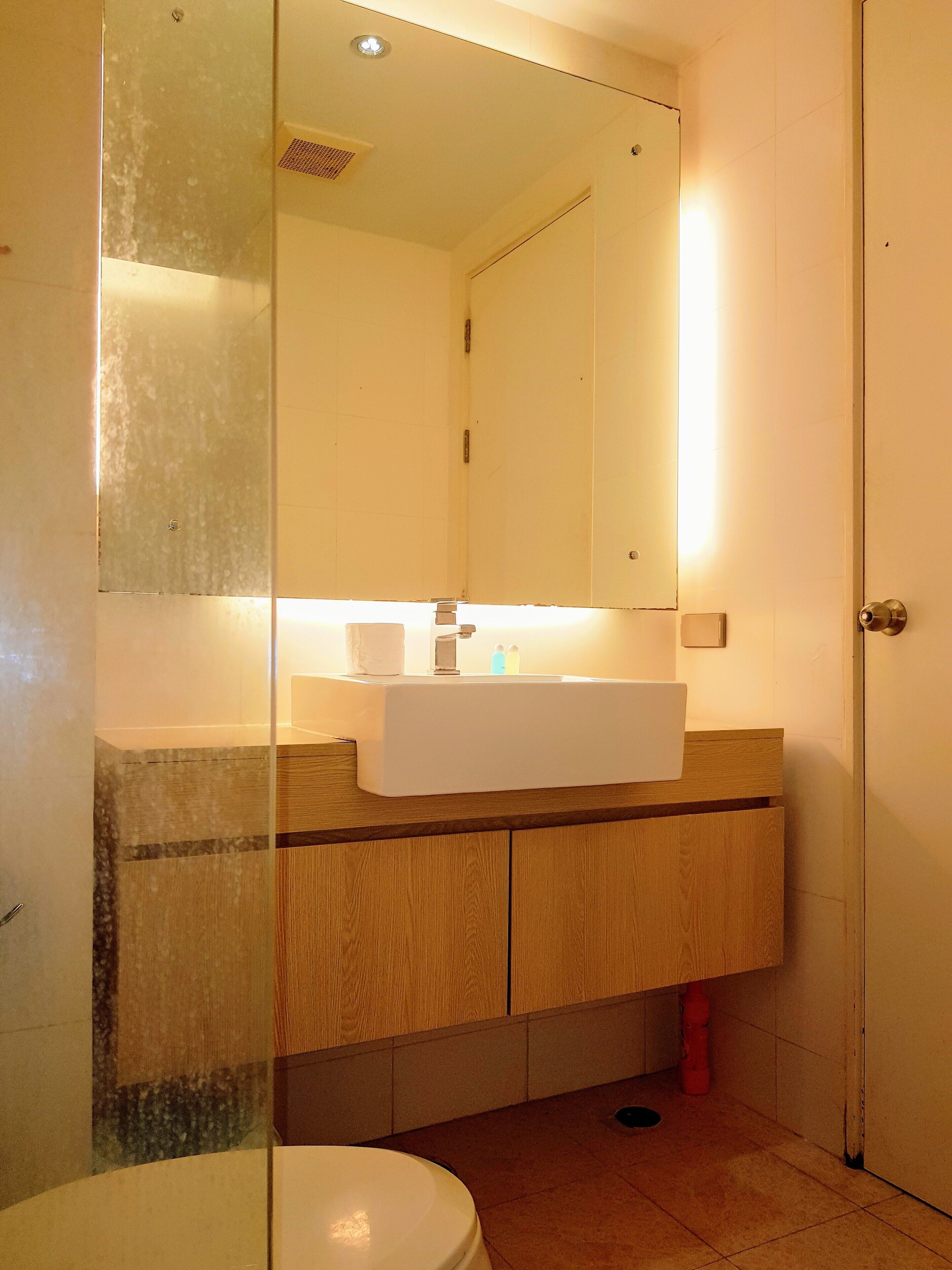 A bathroom with a white sink, wooden cabinets, a mirror, and a toilet.