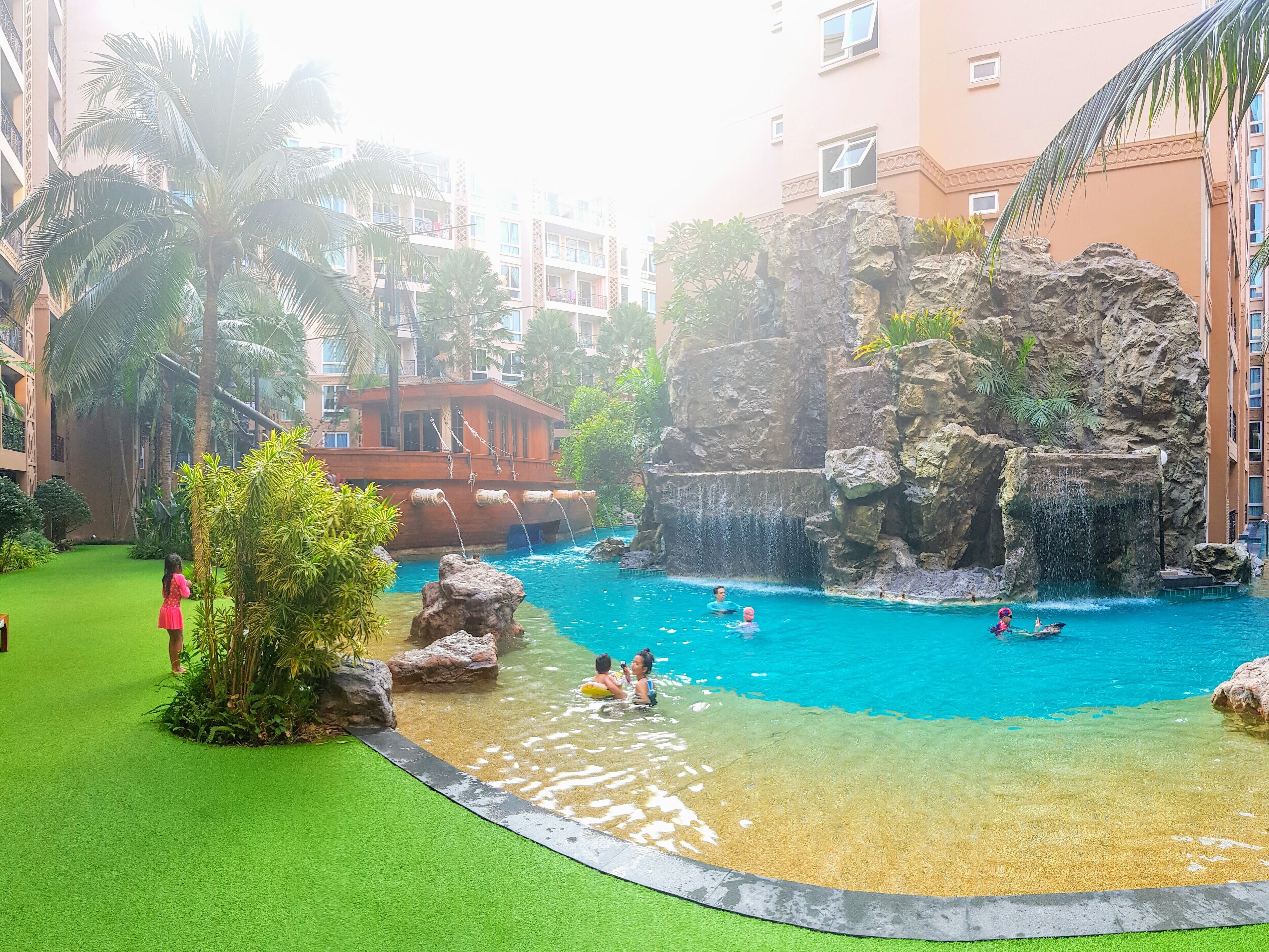 A swimming pool with clear water, surrounded by greenery and a rock formation.