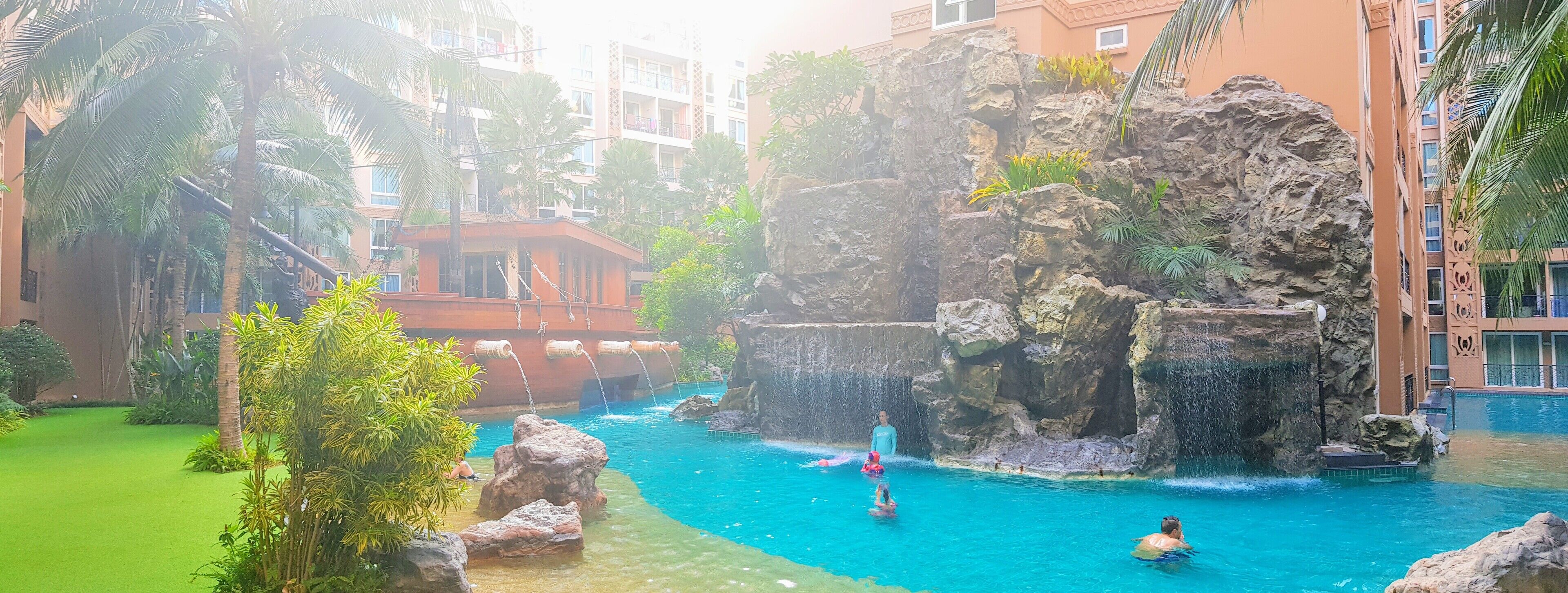 A pool area with clear water, surrounded by tropical plants and a rocky waterfall feature.