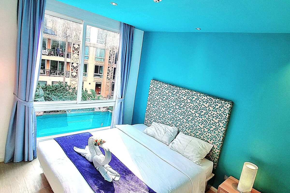 Une chambre avec un grand lit, une vue sur la piscine et un mur d’accent bleu.