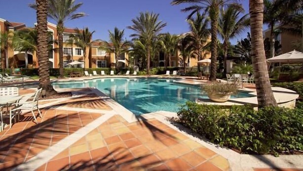 A pool area with lounge chairs and palm trees. - Large fully furnished, quiet condo with lake view, pool and tennis court (Naples)