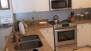 A modern kitchen with white cabinets, stainless steel appliances, granite countertops, and a sign that says "Eat Drink Be Merry". - Large fully furnished, quiet condo with lake view, pool and tennis court (Naples)