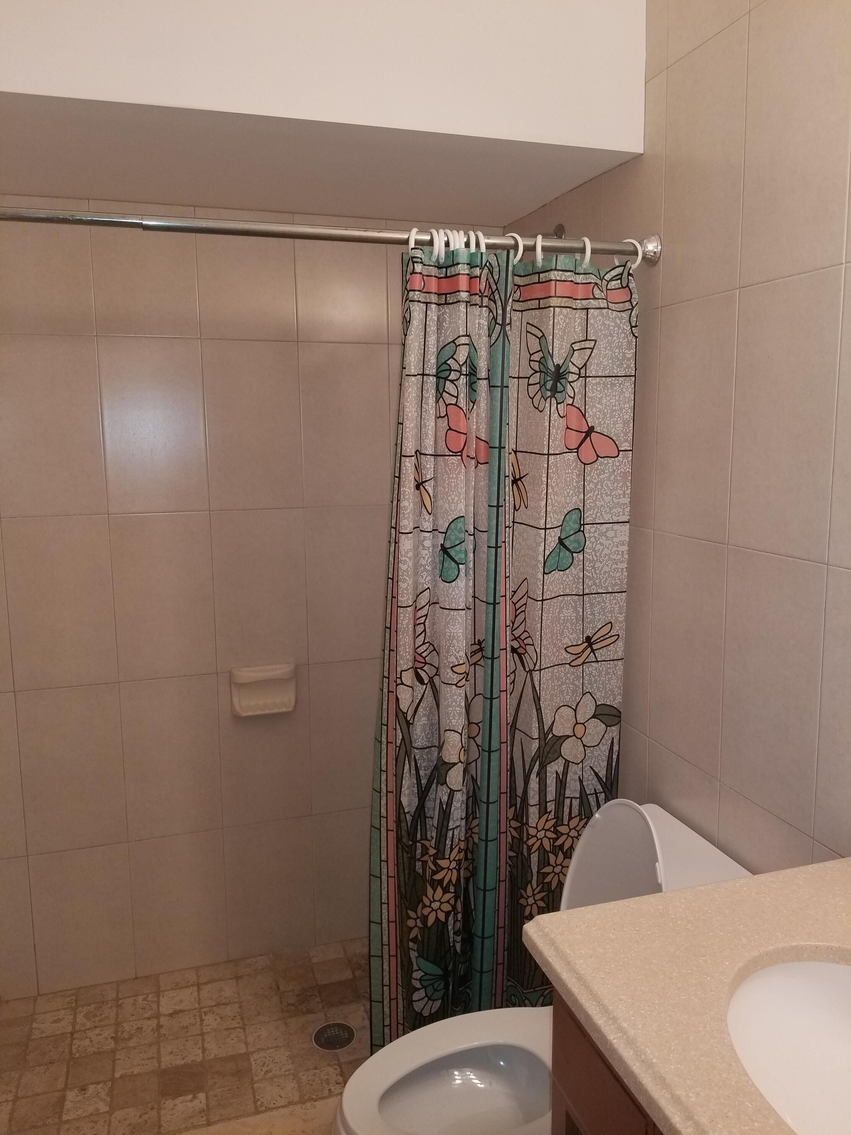 A bathroom with a shower curtain featuring floral and butterfly designs, a toilet, and a sink with a beige countertop.