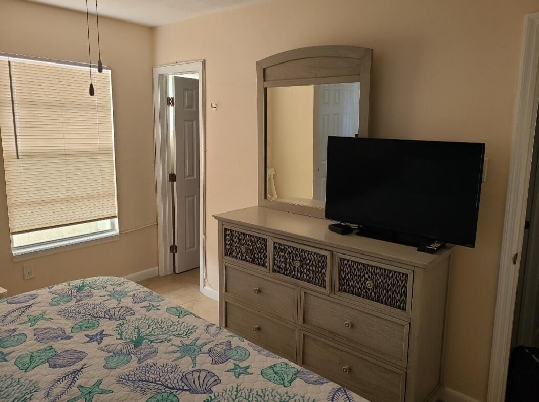 A bedroom with a bed, a dresser, a television, and a window with blinds.