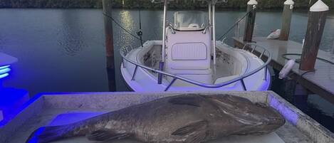 A large fish on a cutting board at a marina with a boat docked in the background.
