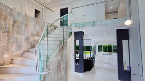 Un intérieur moderne avec un escalier en verre, des murs en marbre et une vue sur un espace extérieur.
