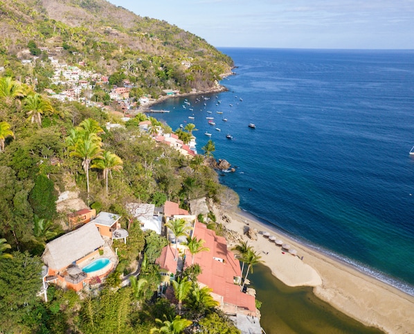 A coastal area with a beach, clear blue sea, and houses with red roofs.
