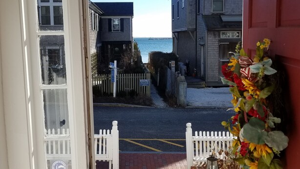 A view through a door to a street with a white picket fence, a brick pathway, and a building with a sign that reads "BEACHCIRCLE." - Spacious 1 Bedroom, First Fl., Beach Access, in quiet East End. 
 (Provincetown)