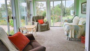 Een kamer met een plafondventilator, een bruine bank met een rode kussen, een bank met bloemenprint en een tafel met stoelen.