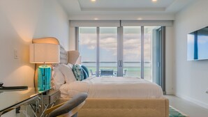 Ein modernes Schlafzimmer mit einem großen Bett, einem Schminktisch mit Spiegel und Meerblick durch große Fenster.