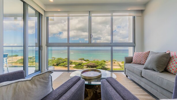 Ein modernes Wohnzimmer mit großem Fenster und Blick auf eine malerische Landschaft, einem grauen Sofa und einem runden Couchtisch.