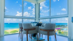 Ein Zimmer mit großen Fenstern und Blick auf einen Strand, zwei graue Stühle und ein kleiner Tisch.