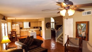 A spacious living room with a ceiling fan, a dining area with a table and chairs, a kitchen with wooden cabinets, and a staircase leading to another level. - Charming Southwest Style Vacation Home  (Phoenix)