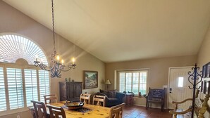 A spacious dining area with a wooden table and chairs, a chandelier, and large windows with blinds. - Charming Southwest Style Vacation Home  (Phoenix)