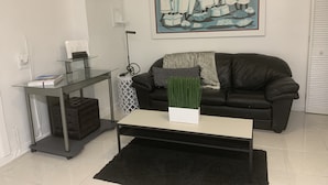 Un saló modern amb una taula de centre de vidre, un sofà negre, un quadre a la paret i una petita taula auxiliar amb una làmpada.