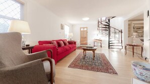 A spacious living room with a red sofa, a wooden chair, a coffee table, and a spiral staircase. - Spacious Family House in Barnes, 30 Minutes from Downtown London (London)