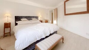 A bedroom with a large bed, two bedside tables with lamps, a bench, and a large mirror on the wall. - Spacious Family House in Barnes, 30 Minutes from Downtown London (London)