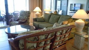 A living room with a green sofa, a wicker chair, a glass coffee table, and two lamps. - 1 month minimum, waterfront, see dolphins, pool/hot tub (Saint Petersburg)