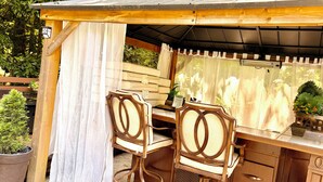A wooden outdoor seating area with two chairs and a table, surrounded by a covered structure with a window. - Atlanta Pool Home Near Airport, Near Airport 8 guests Max (Atlanta)