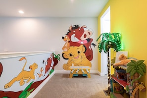 A children's playroom with a mural of animated characters, a wooden play table, and a bookshelf with plush toys. - Sunny Home with Themed Rooms in Encore (Kissimmee)