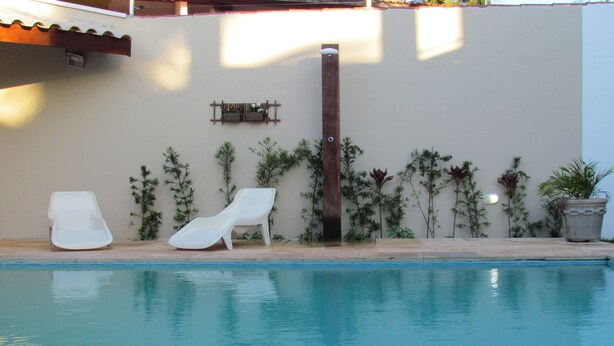 Une piscine avec deux chaises longues blanches et une plante en pot.
