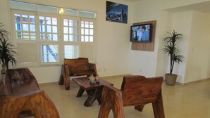 Un salon spacieux avec une table basse en bois, deux chaises en bois, un canapé et un téléviseur fixé au mur.
