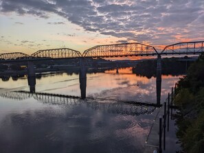 A bridge over a calm river at sunset with industrial structures in the background.