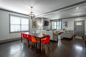 A spacious living area with a dining table, bright orange chairs, a gray sofa, and a gray couch.