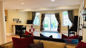 A living room with a sofa, red and brown cushions, a piano, and a dining area with a table and chairs. - 10 mins. to downtown Saratoga and SPAC. 1,000 sq. ft. Spacious and quiet. (Ballston Spa)