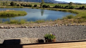 Une vue sur un lac, avec des montagnes en arrière-plan, un chemin de gravier et une terrasse en bois agrémentée de plantes en pot.