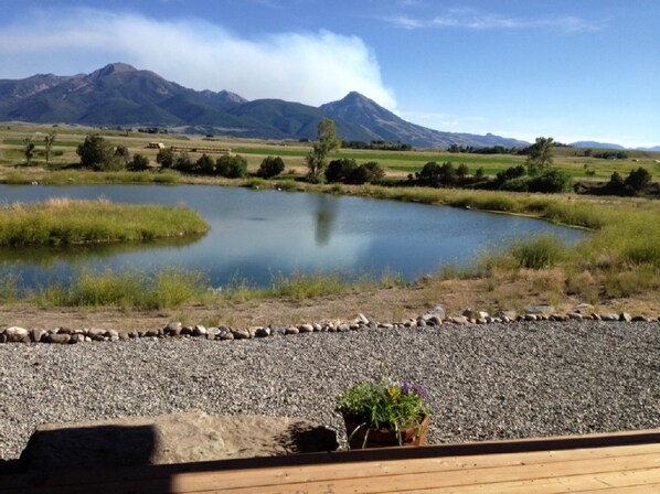 A view of a lake with mountains in the background, a gravel path, and a wooden deck with potted plants.