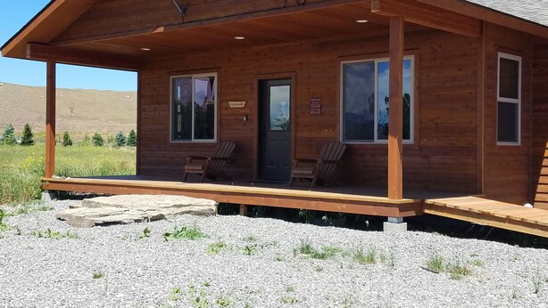 Une cabane en bois avec une véranda, deux chaises, une porte et une pancarte sur laquelle on peut lire : « Détendez-vous ».